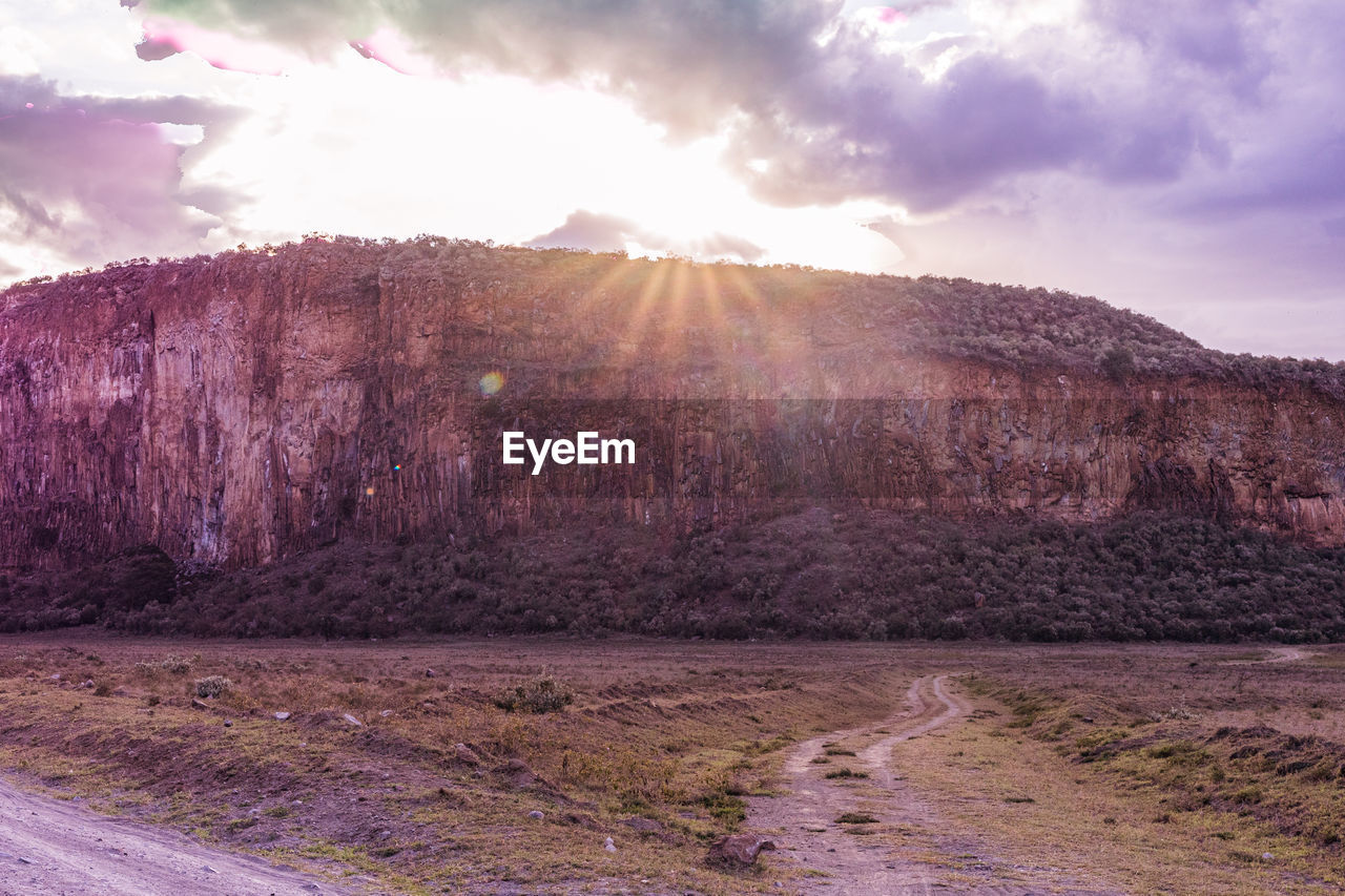 sky, cloud, landscape, environment, nature, land, scenics - nature, mountain, beauty in nature, sun, plateau, travel, travel destinations, no people, sunset, sunlight, sunbeam, rock, wilderness, outdoors, plant, non-urban scene, tranquility, lens flare, valley, tree, tourism, purple, multi colored, road, dramatic sky, tranquil scene, geology, day