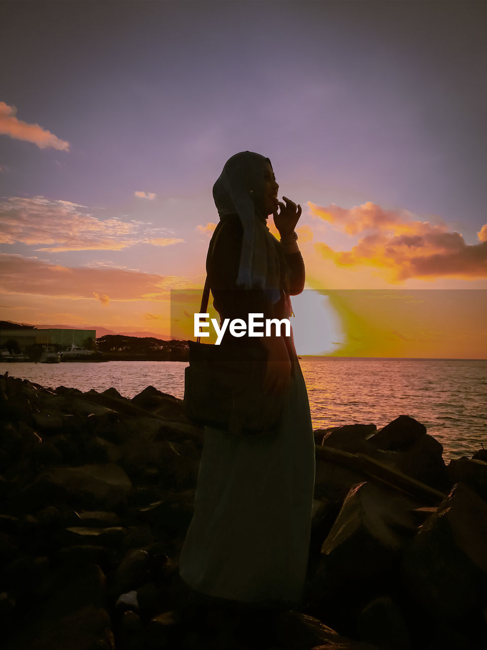 Woman photographing sea against sky during sunset