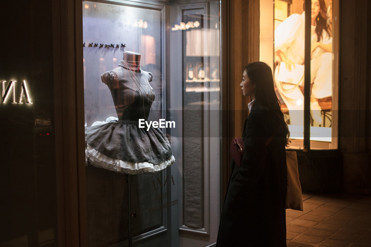 REAR VIEW OF WOMAN STANDING BY WINDOW IN STORE