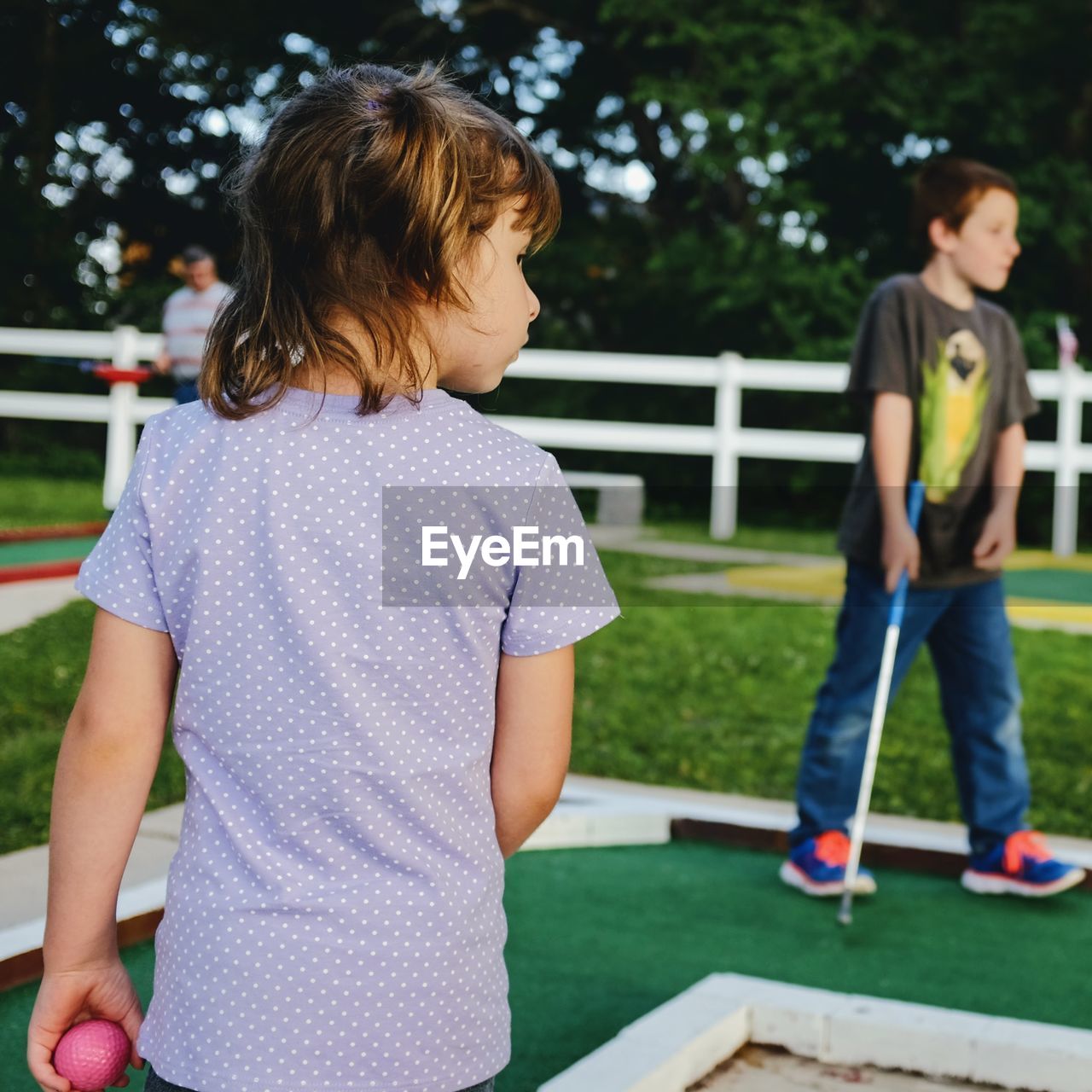 Rear view of girl with brother playing miniature golf at lawn
