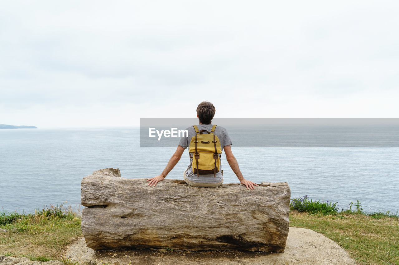 rear view of woman standing on rock at beach against sky