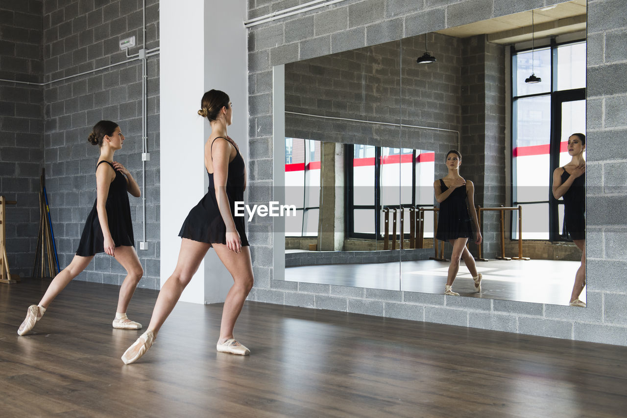 Couple of young woman dancers doing a stretching routine in front of a mirror at dance studio