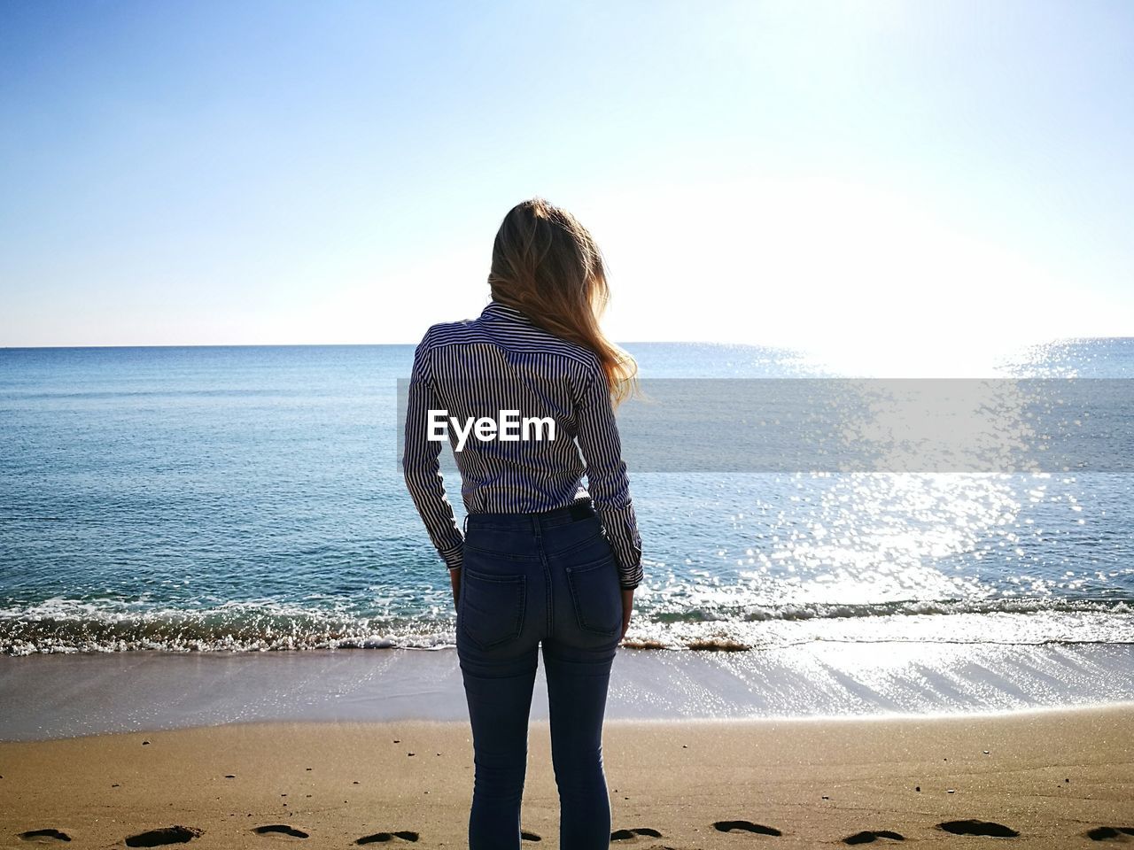 Rear view of woman standing on sea shore at beach against clear sky