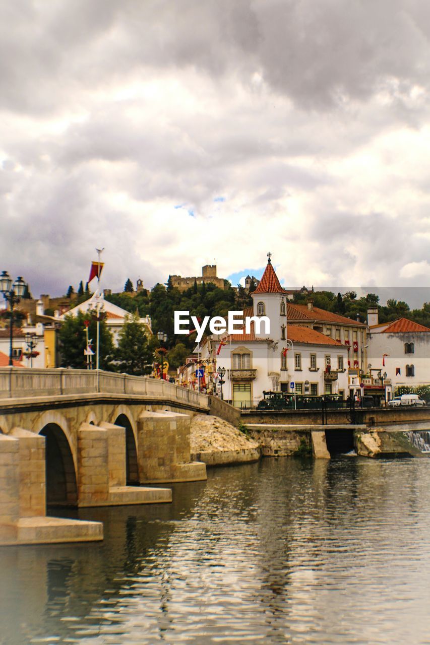 RIVER WITH BUILDINGS IN BACKGROUND AGAINST CLOUDY SKY