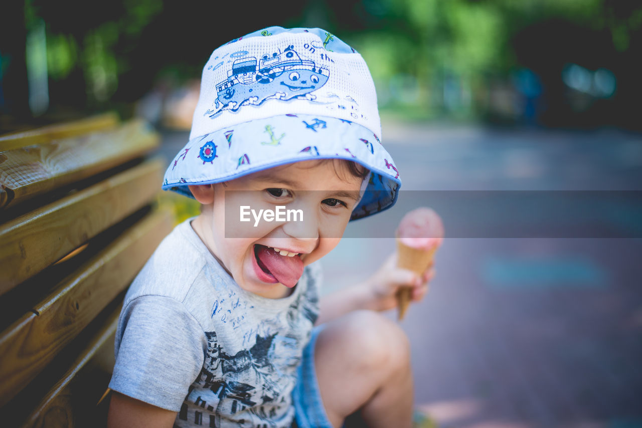 Portrait of cheerful boy eating ice cream while sitting on park bench