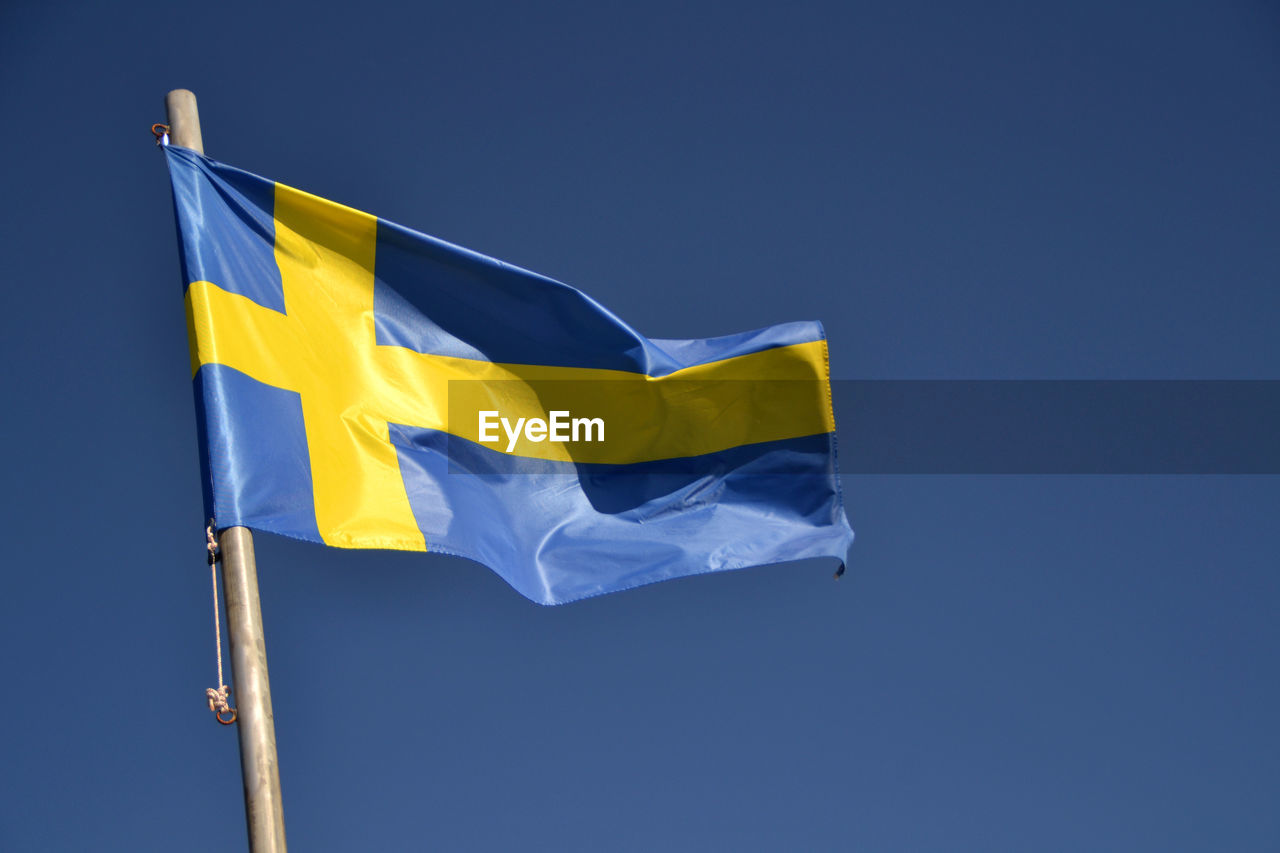 Low angle view of swedish flag against blue sky