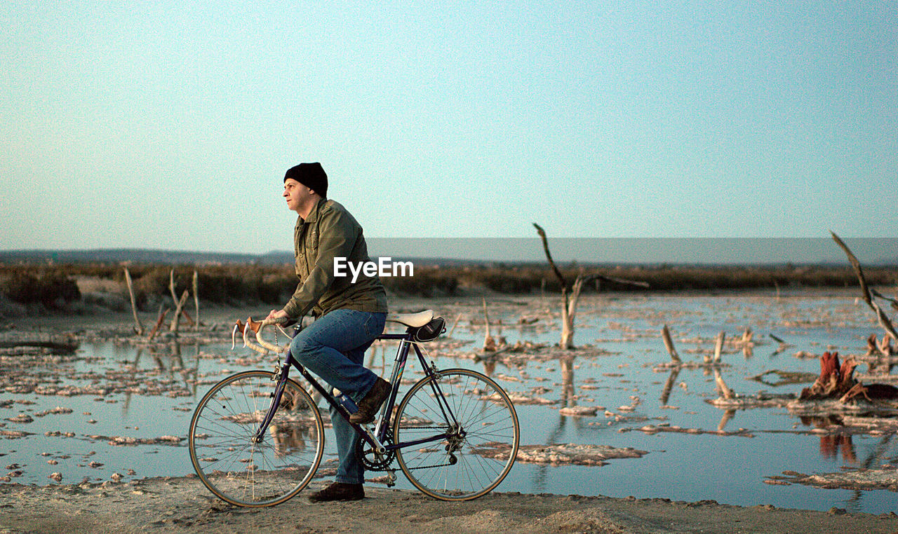 Man with bicycle standing at lake against clear sky