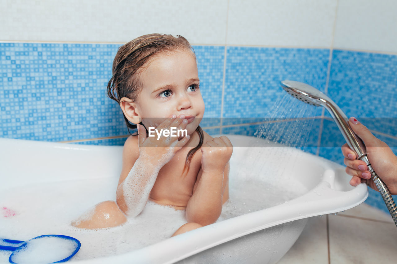 Cropped hand bathing girl in bathroom at home