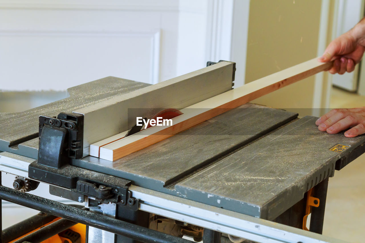 Cropped hands of worker cutting plank with electric saw in workshop