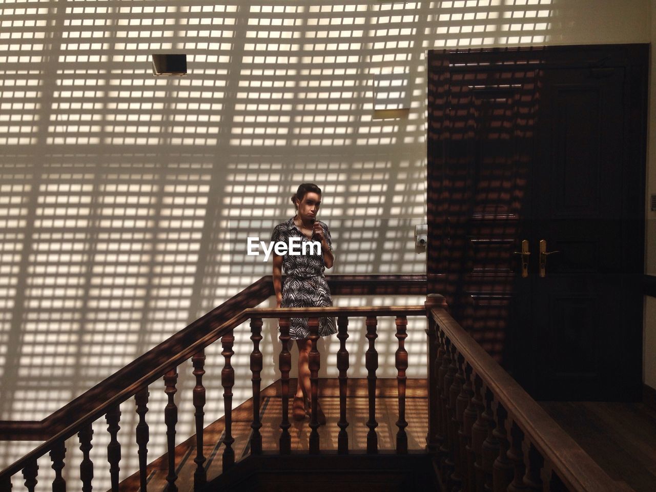 Portrait of young woman standing at stairway while shadow falling on wall