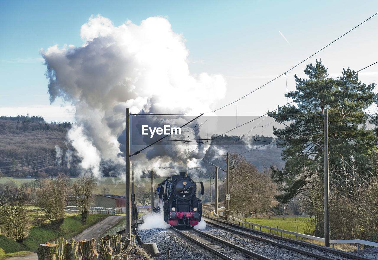 TRAIN ON RAILROAD TRACK BY MOUNTAIN AGAINST SKY