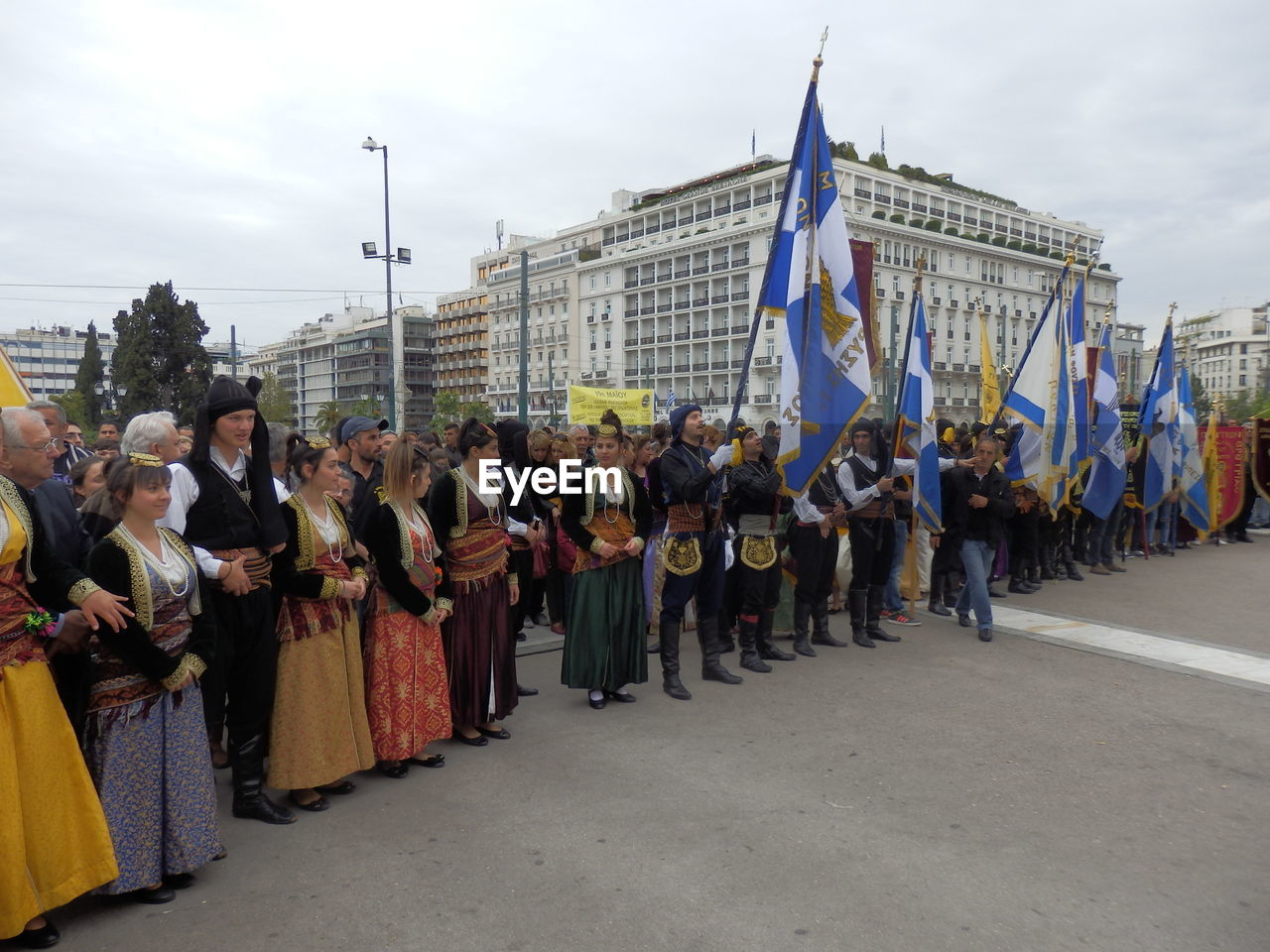 People in traditional clothing with flags standing on road in city