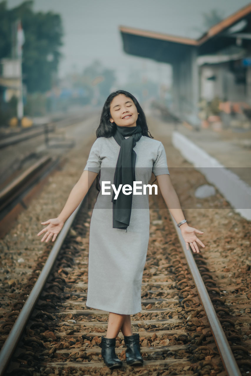 PORTRAIT OF YOUNG WOMAN STANDING ON RAILROAD TRACK