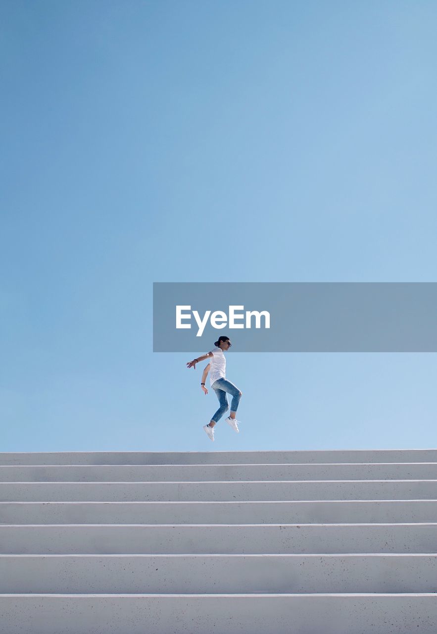 Low angle view of person jumping against clear sky