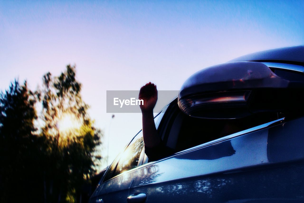 Low angle view of hand on car window against sky during sunset