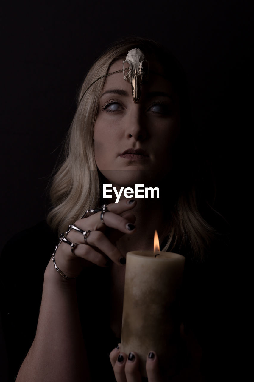 Portrait of spooky woman holding lit candle against black background