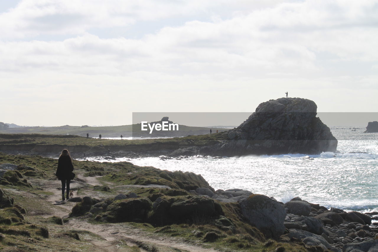 REAR VIEW OF PEOPLE LOOKING AT SEA SHORE