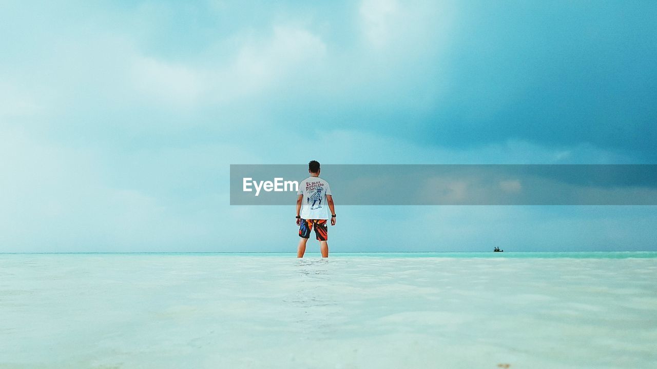 REAR VIEW OF MAN STANDING IN SEA