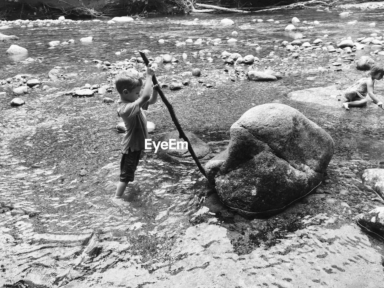 Boy holding stick while standing in river