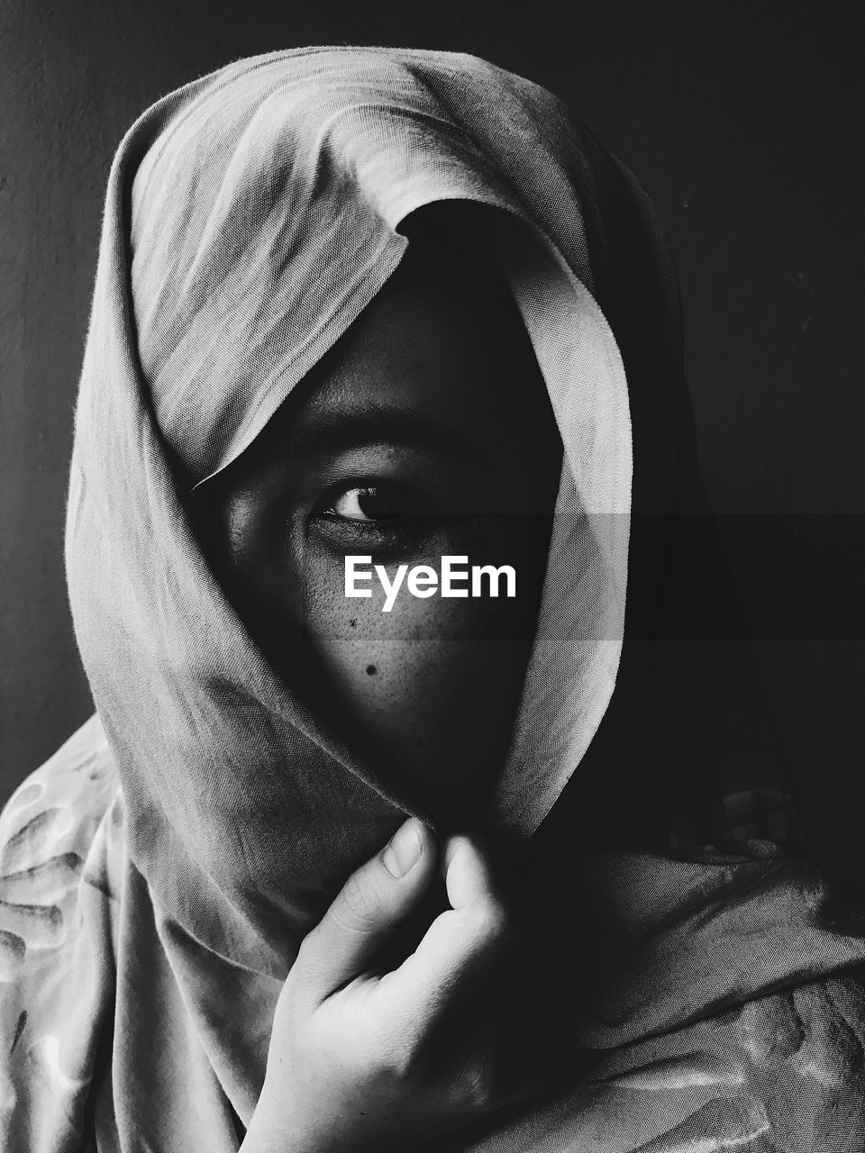 Close-up portrait of young woman wearing scarf against black background