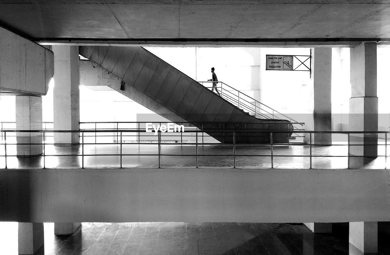 MAN WALKING ON STAIRCASE OF BRIDGE AGAINST BUILDING