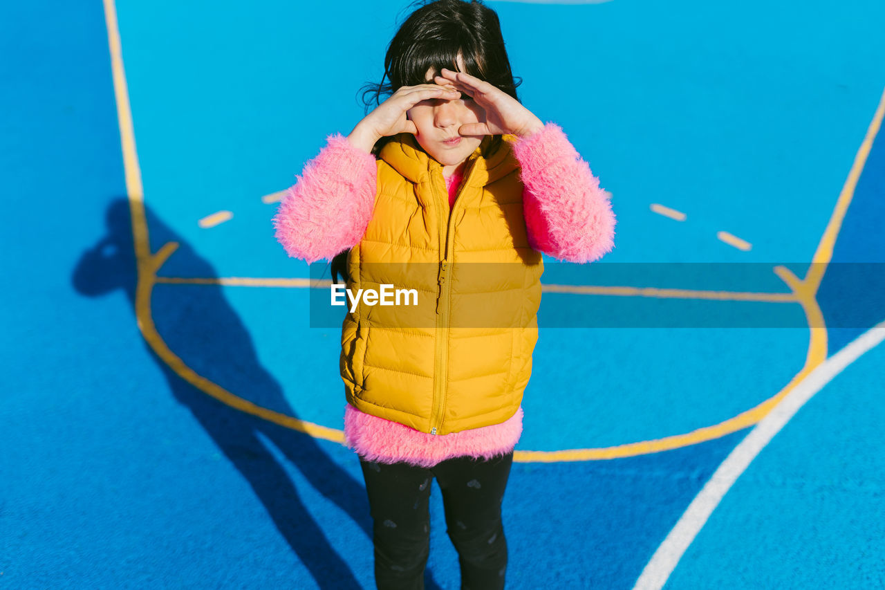 Girl shielding eyes while standing at basketball court on sunny day