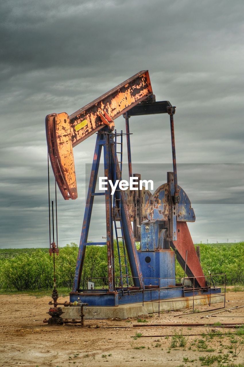 Rusty abandoned oil rig on field against cloudy sky