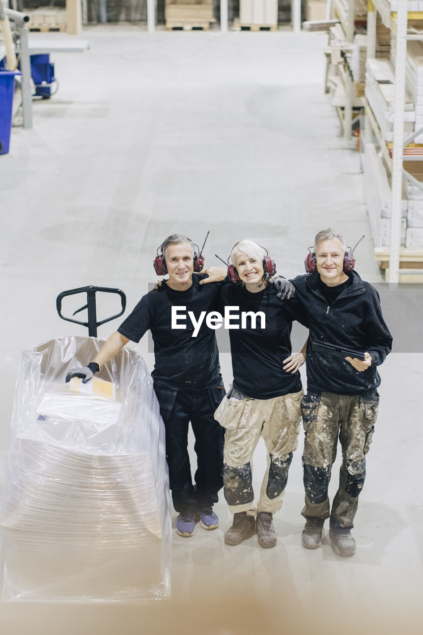 High angle portrait of smiling male and female workers standing with pallet jack in industry