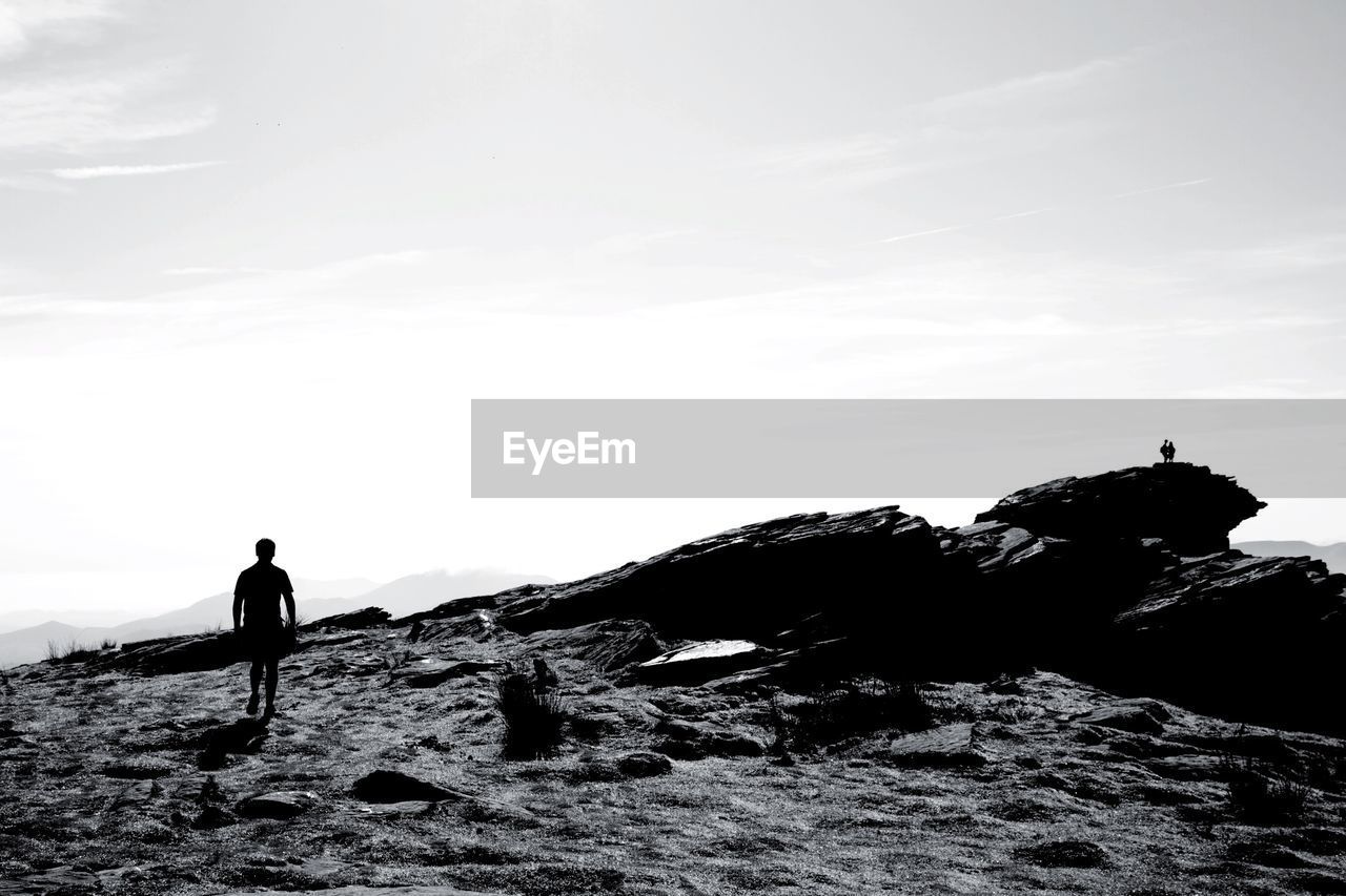 Man walking on rocky landscape against sky