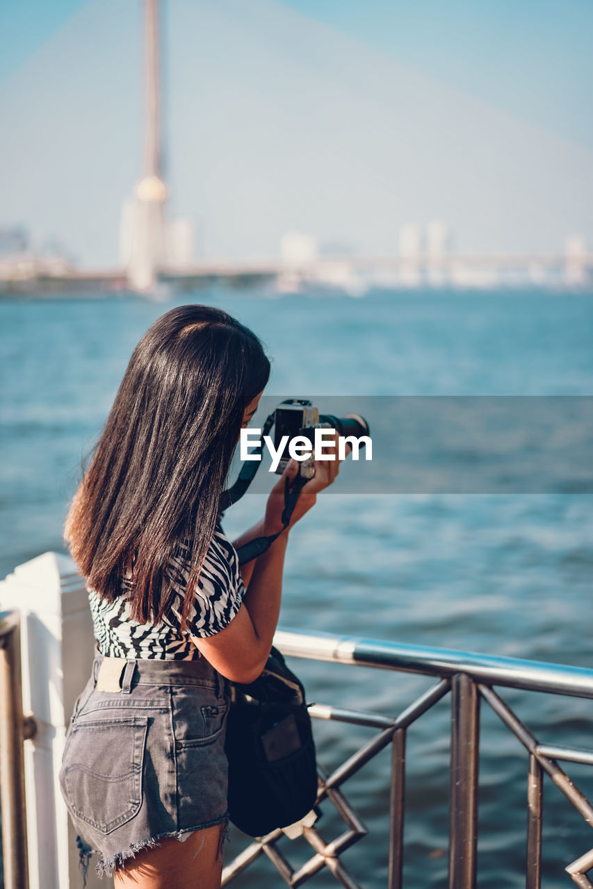 Rear view of woman photographing against sea