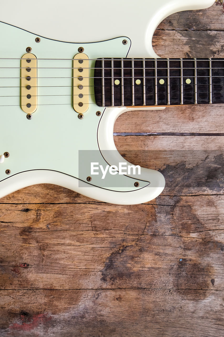 Detail of white electric guitar on a wood background.