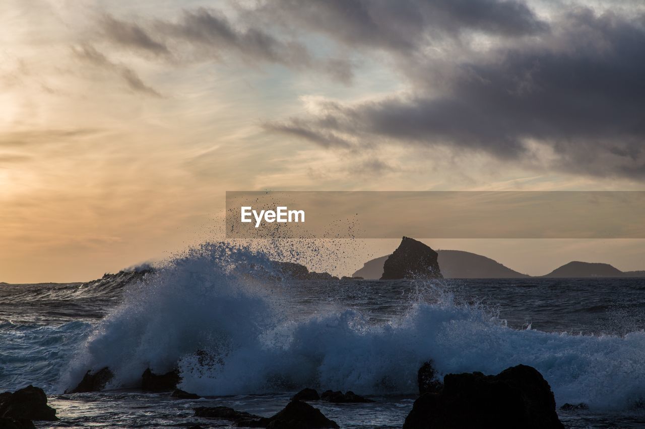 WAVES SPLASHING ON SEA AGAINST SKY