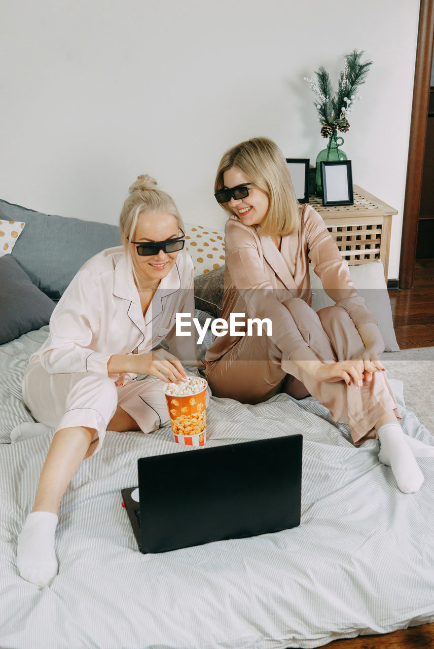 Blondes at home watch movie on laptop with 3d glasses and eat popcorn. concept of friendship