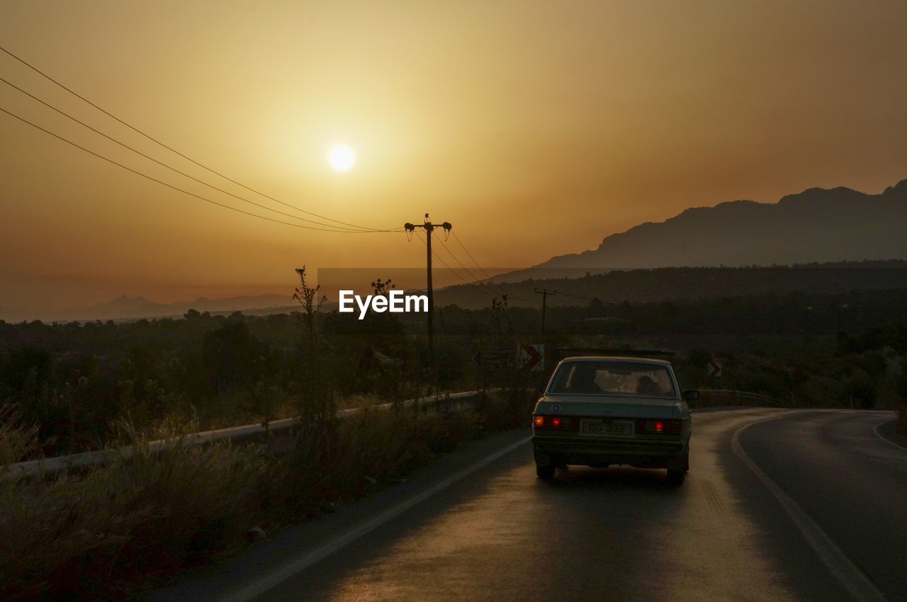 VEHICLES ON ROAD AGAINST SKY DURING SUNSET