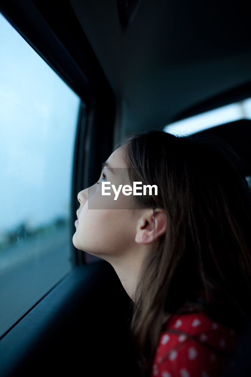 Side view of thoughtful girl looking through car window