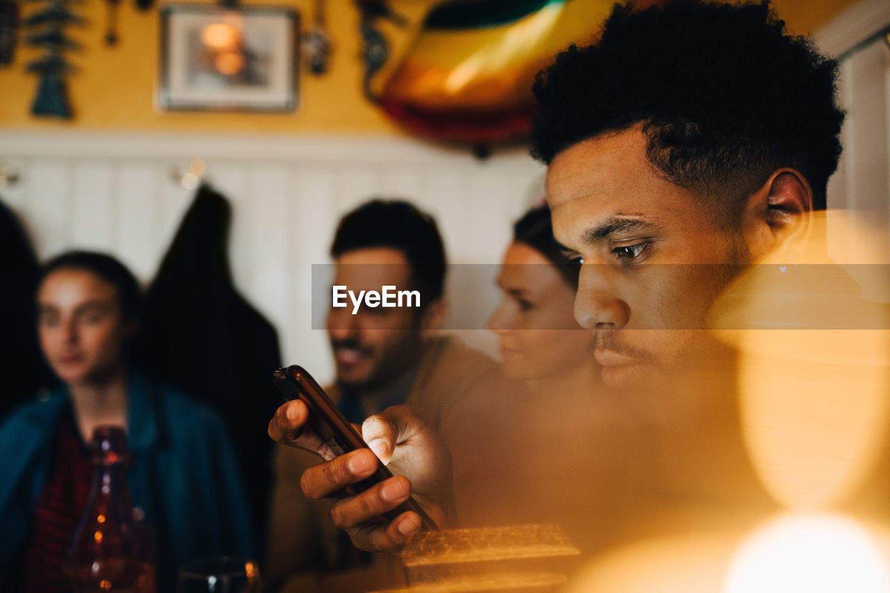 Young man using smart phone while sitting by friends at restaurant during dinner party