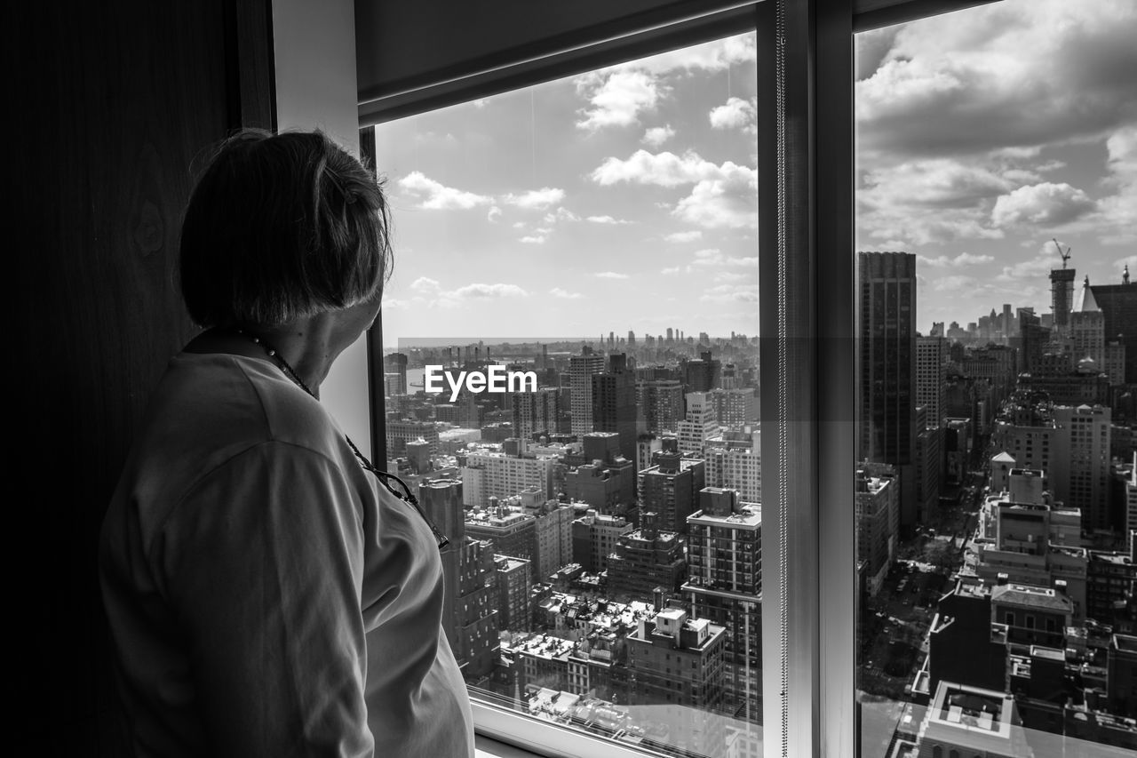 Side view of woman looking at buildings through apartment window