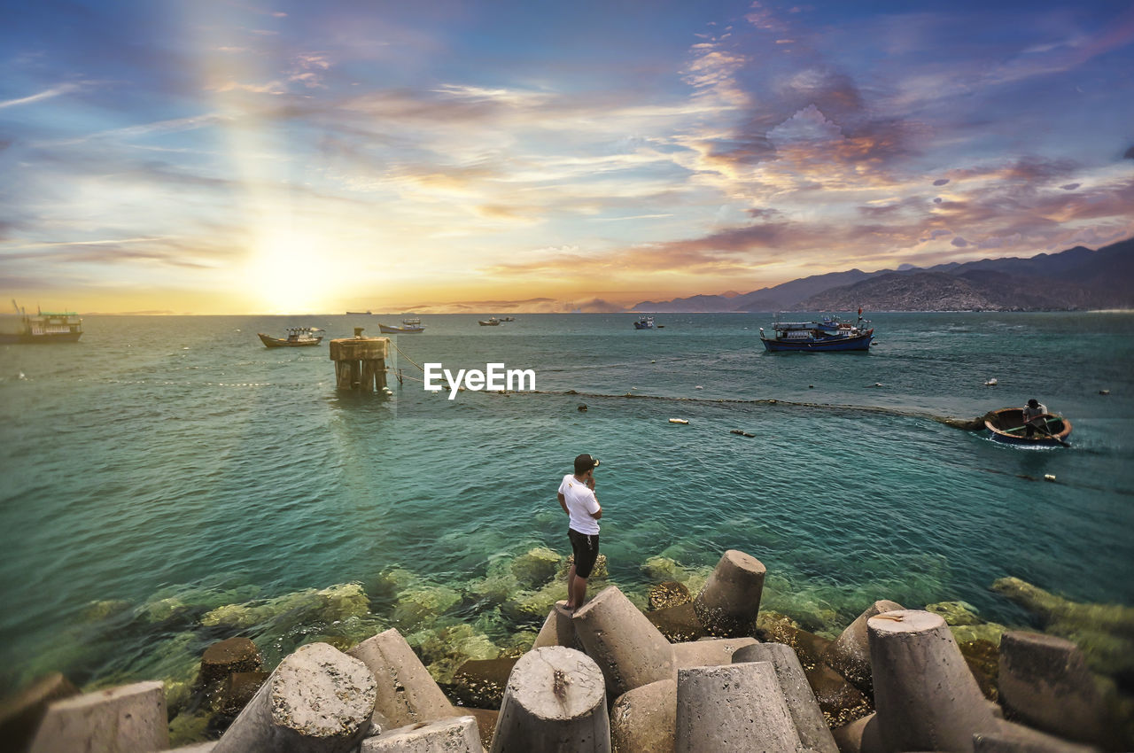 High angel view of man standing on rocks by sea against sky during sunset