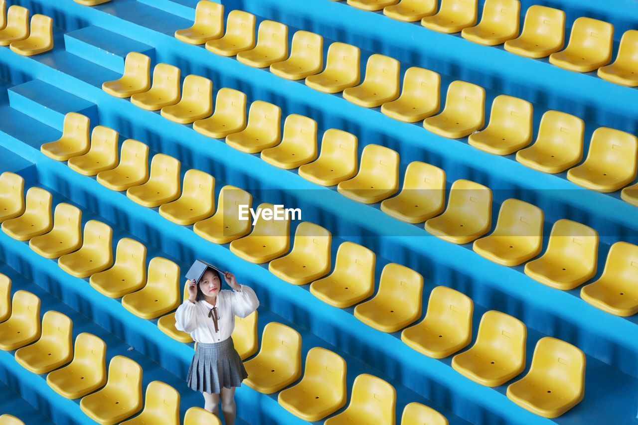 High angle portrait of young woman with book standing in stadium