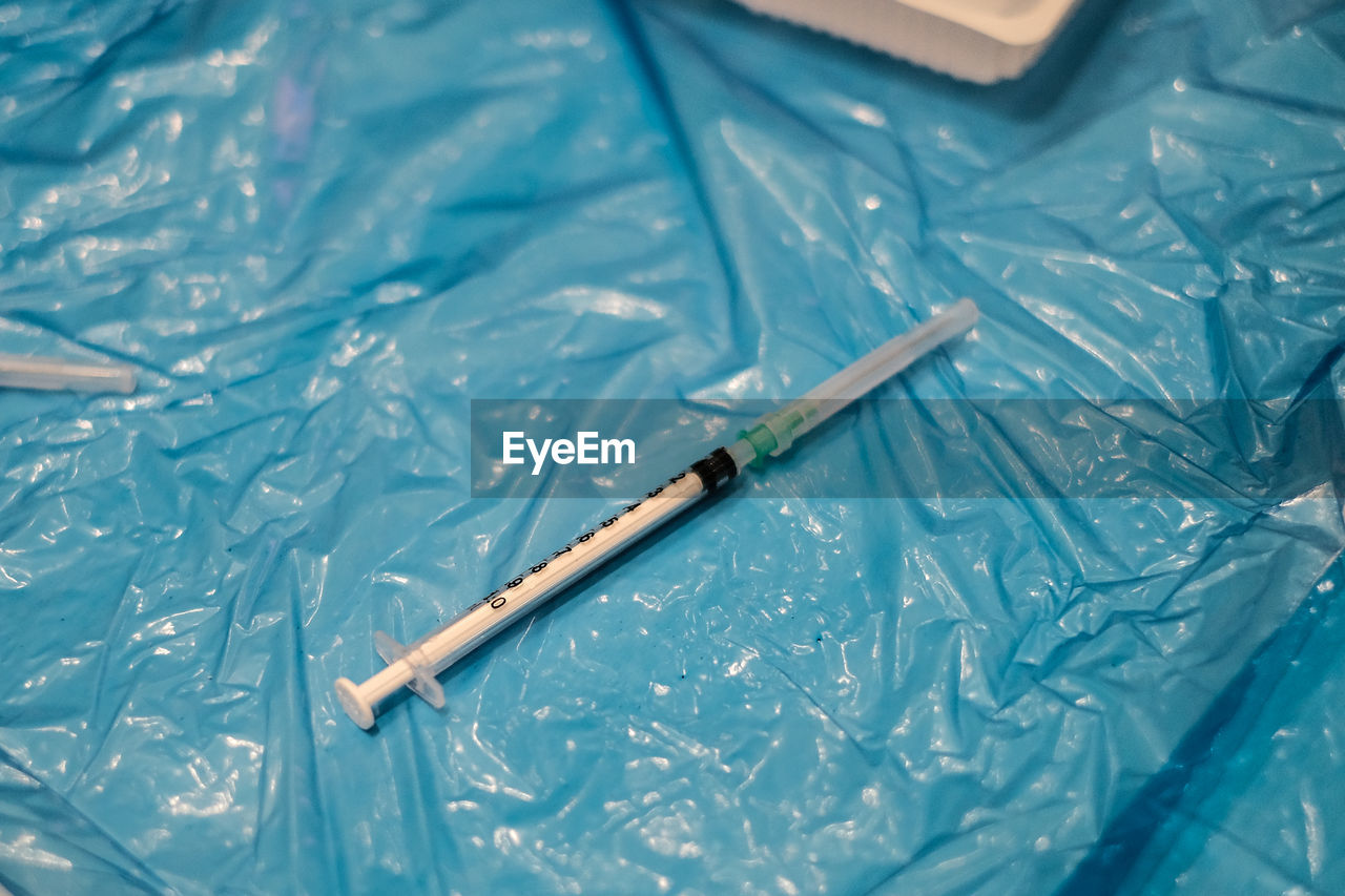 High angle view of a syringe on blue plastic sheet