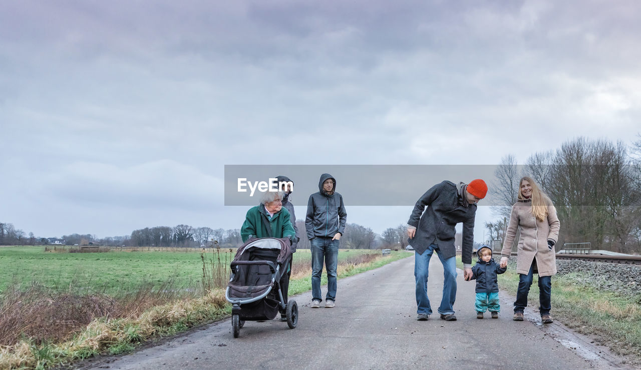 Family walking on road against cloudy sky during winter