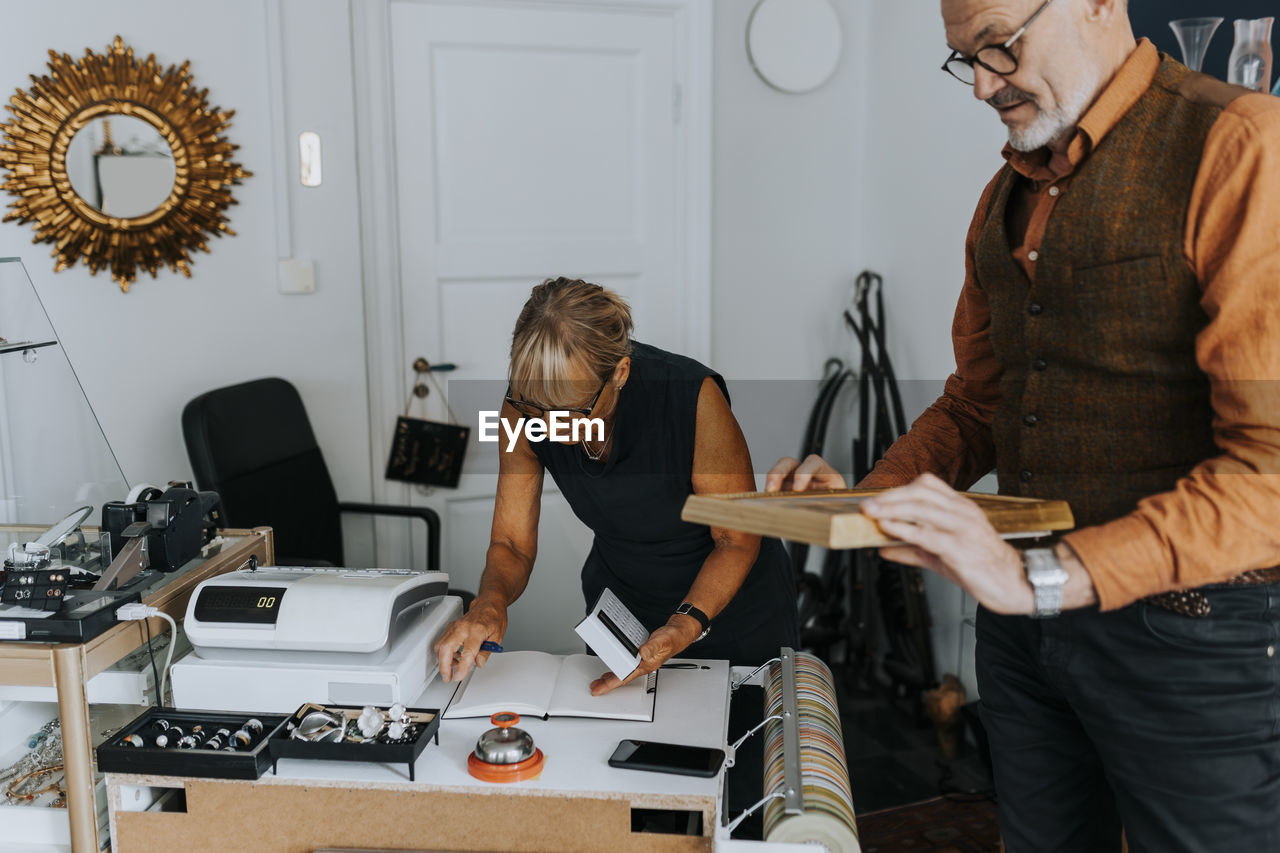 Elderly male entrepreneur examining picture frame by female colleague in antique shop