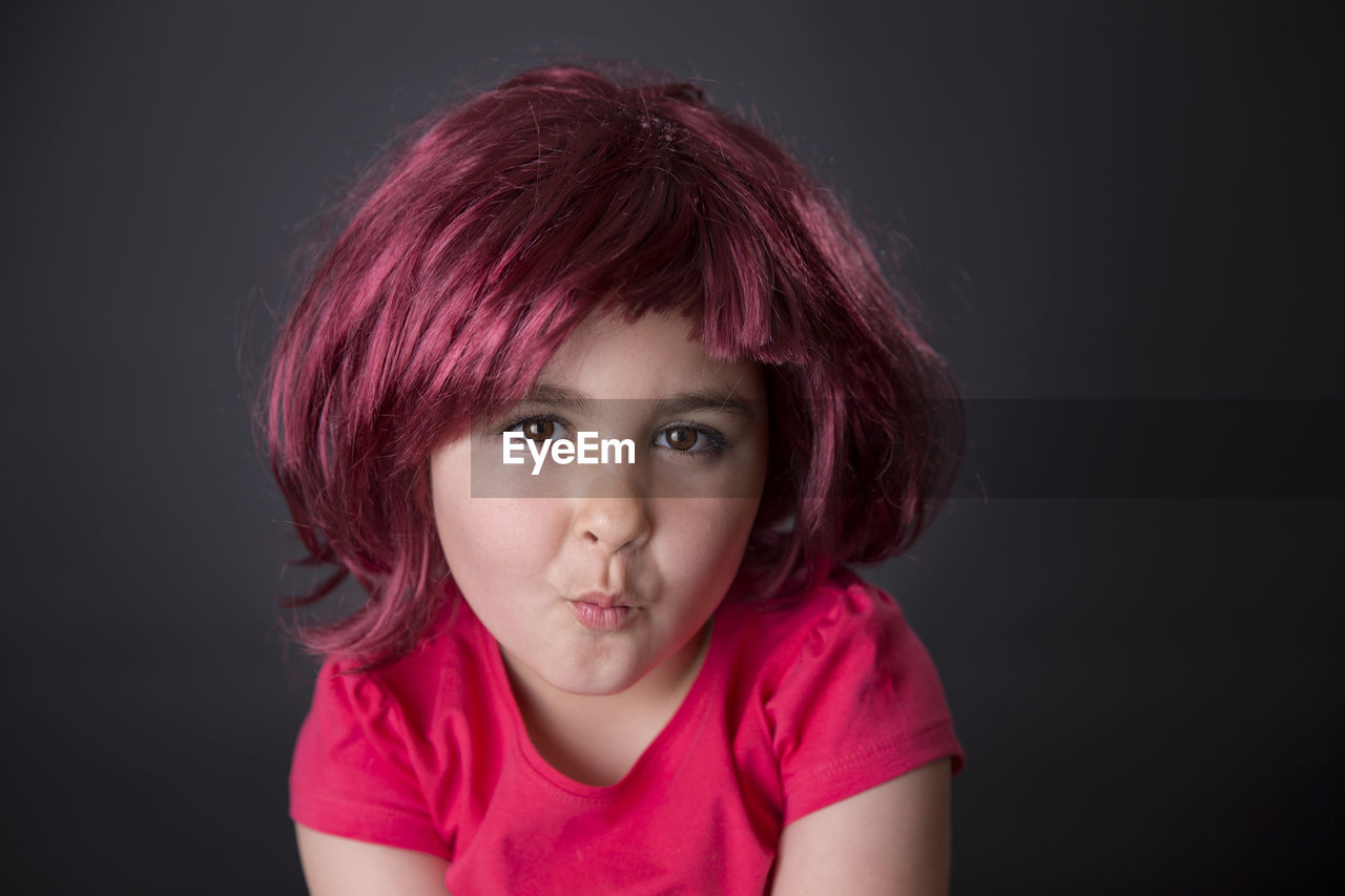Portrait of girl wearing red wig against gray background
