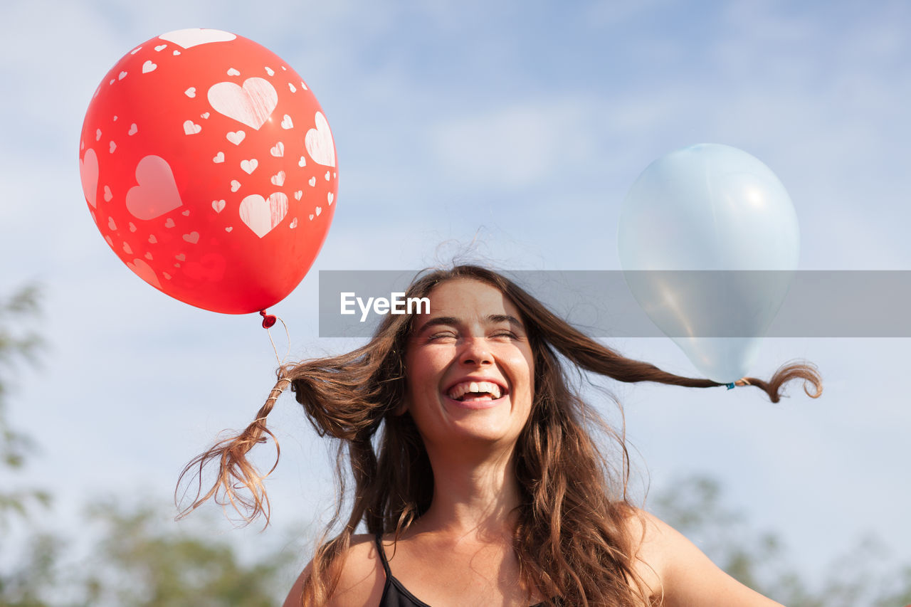 Happy woman tied balloons in hair against sky