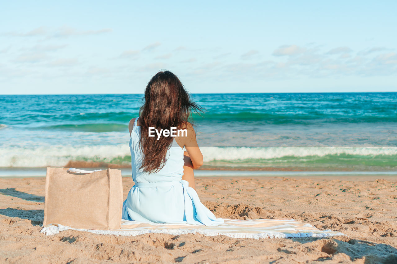 rear view of woman sitting at beach against sky