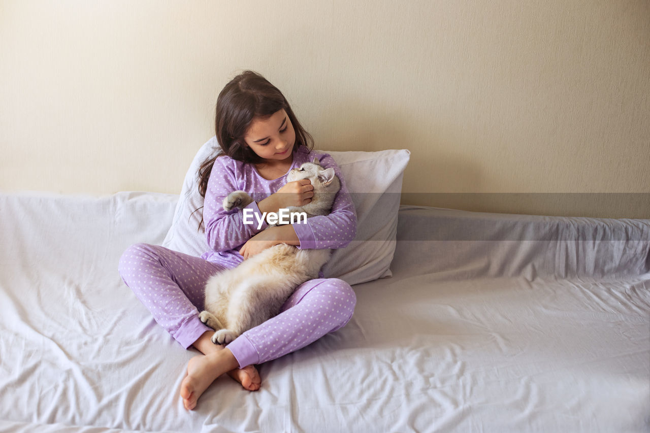 Girl with cat sitting on bed at home