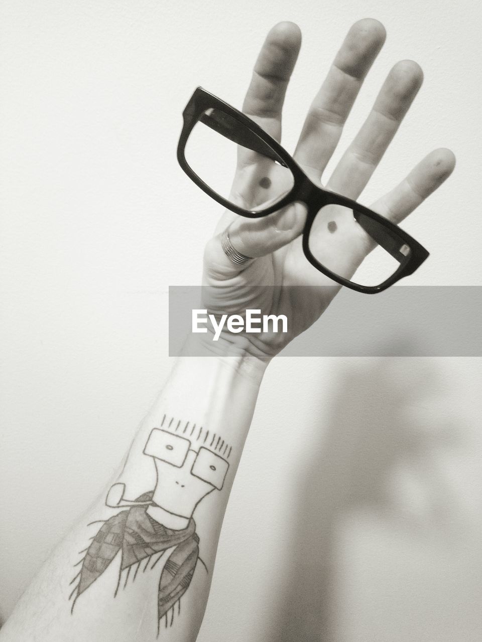 Close-up of human hand with tattoo holding eyeglasses against wall