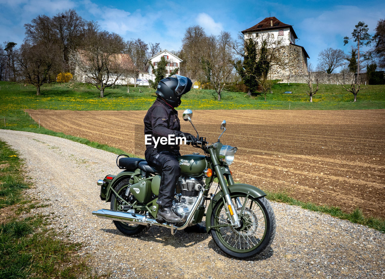 MAN RIDING BICYCLE ON FIELD AGAINST SKY