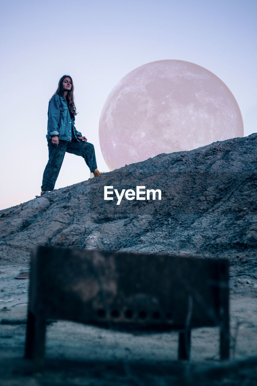 Digital composite image of woman standing against moon on rock formation