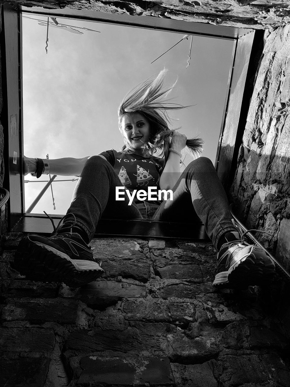 PORTRAIT OF YOUNG WOMAN SITTING AGAINST WALL